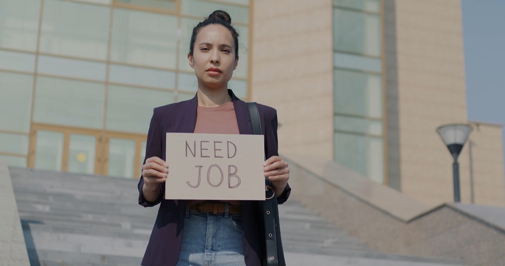 Woman holding a sign that reads "Need Job" while standing on city steps