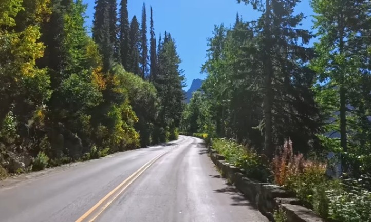 A scenic Sun road lined with trees, leading towards majestic mountains in the background