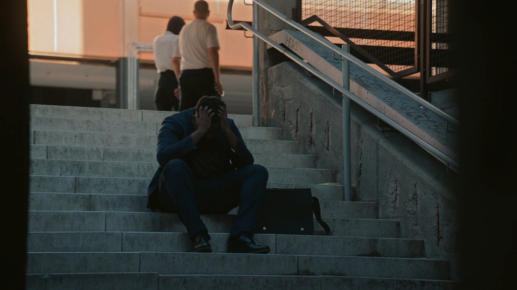 Man in a suit sitting on stairs with head in hands, representing emotional stress linked to unemployment rates