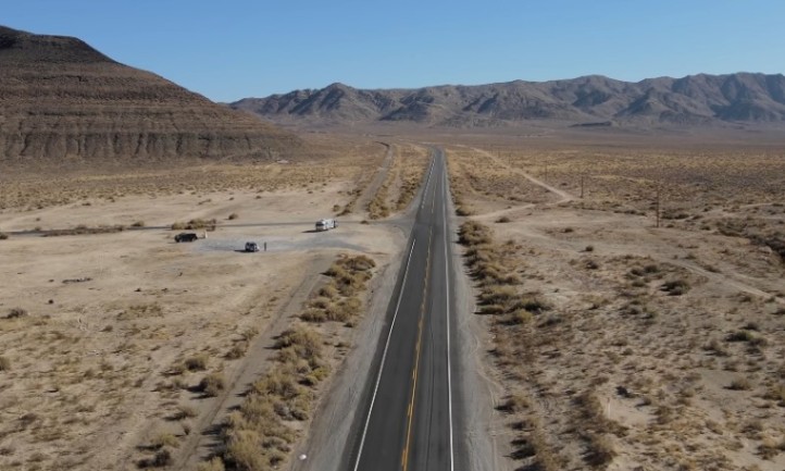 Aerial view of a long, winding highway cutting through a vast, arid desert landscape under a clear blue sky