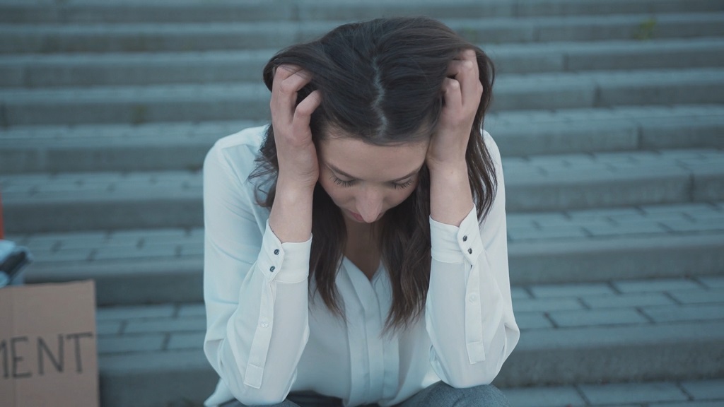 Woman in business attire sitting on steps with head down, visibly distressed