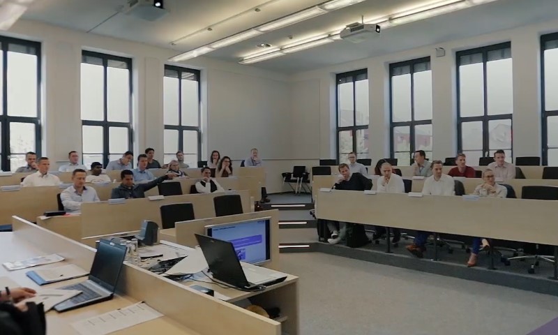A large group of diverse individuals seated in a classroom, engaged in a learning activity