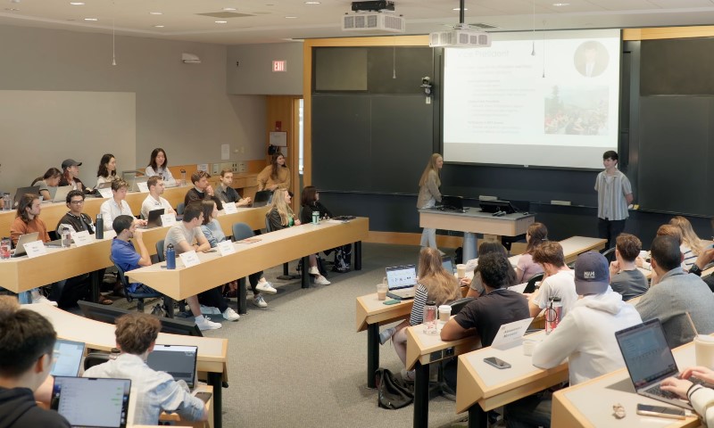 A classroom filled with students seated at desks, using laptops, engaged in learning activities