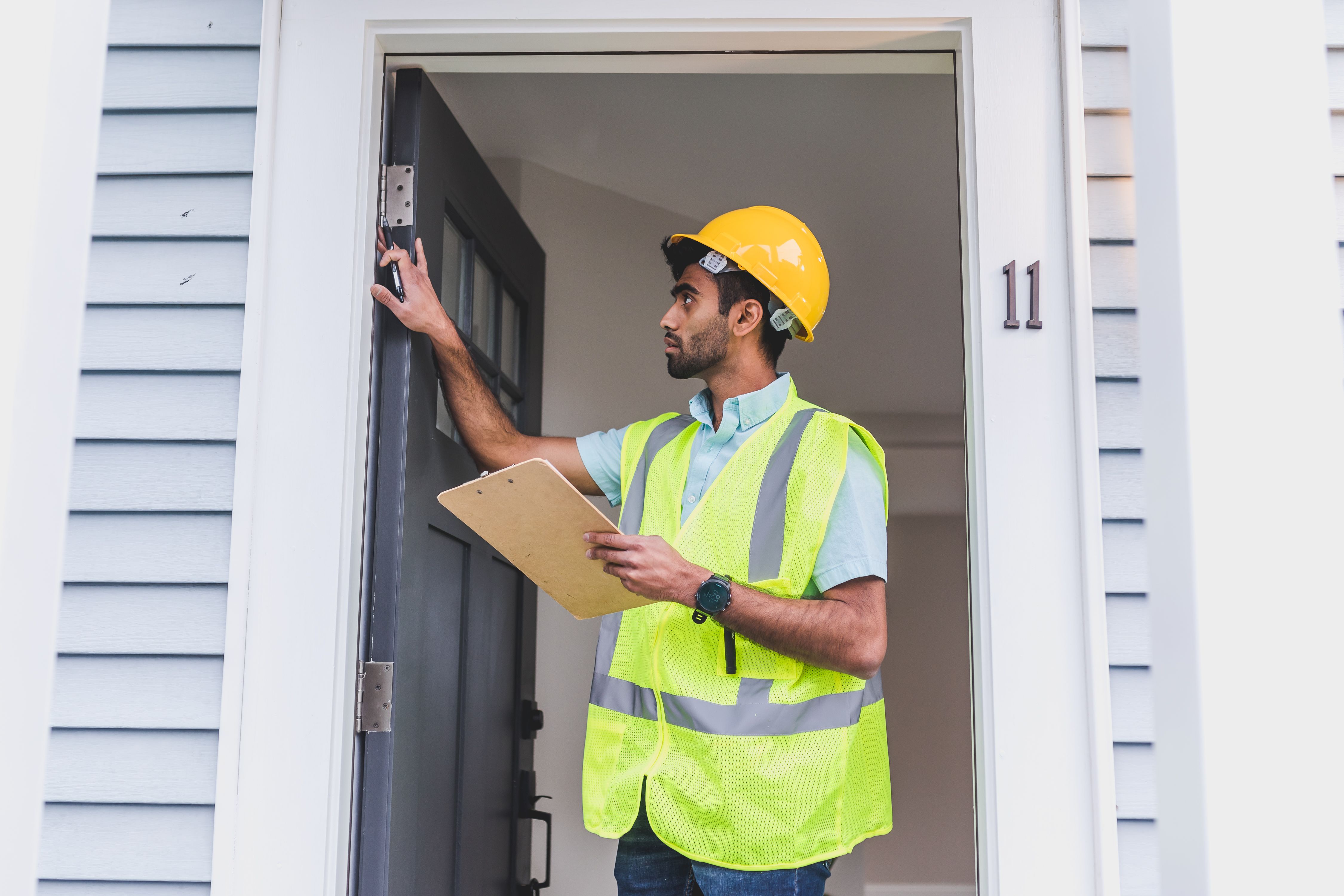 Home inspector in safety vest and hard hat checking a doorframe outdoors with clipboard
